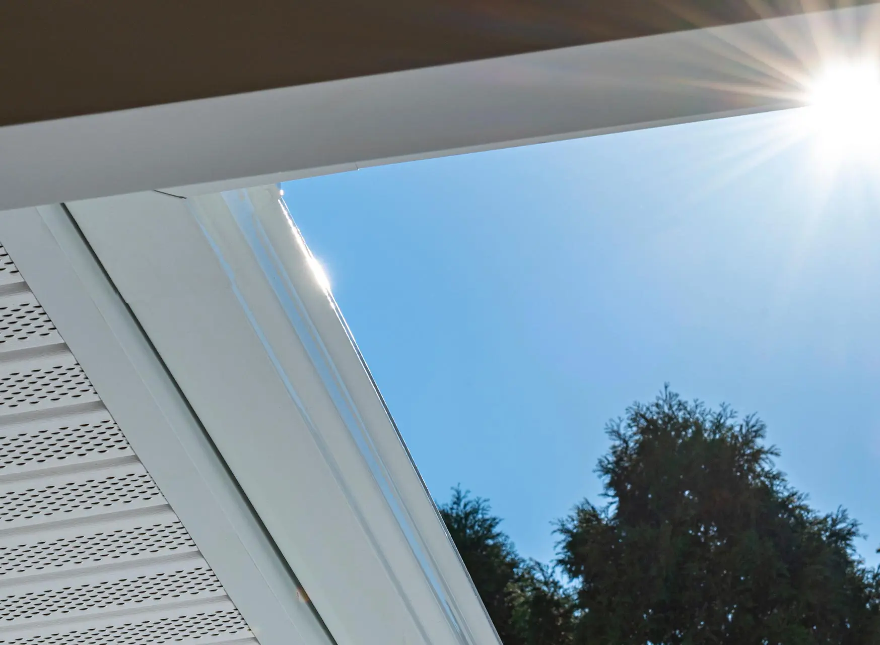 Looking up at newly installed gutters, fascia and perforated soffit – sun flare